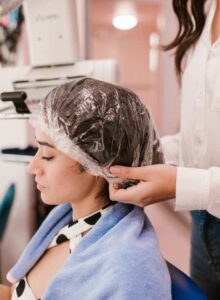 A dark-haired woman wearing a shower cap at salon with eyes closed