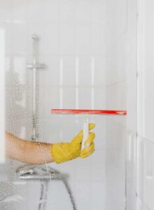 A yellow- gloved hand cleaning Shower Glass door with viper